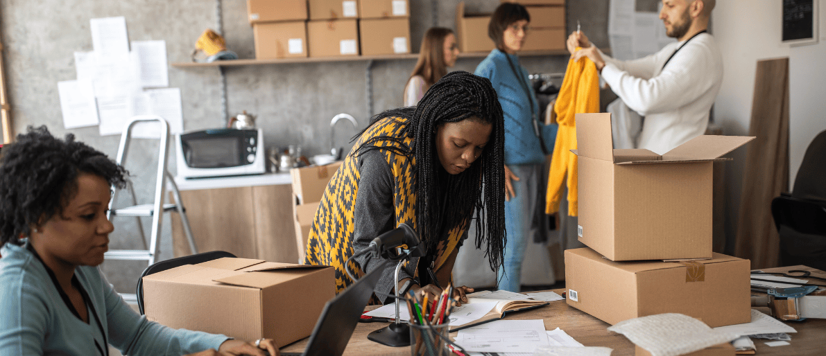 3 Menschen die sich um das E-Commerce kümmern. Sie packen Pakete und bauen einen Onlineshop