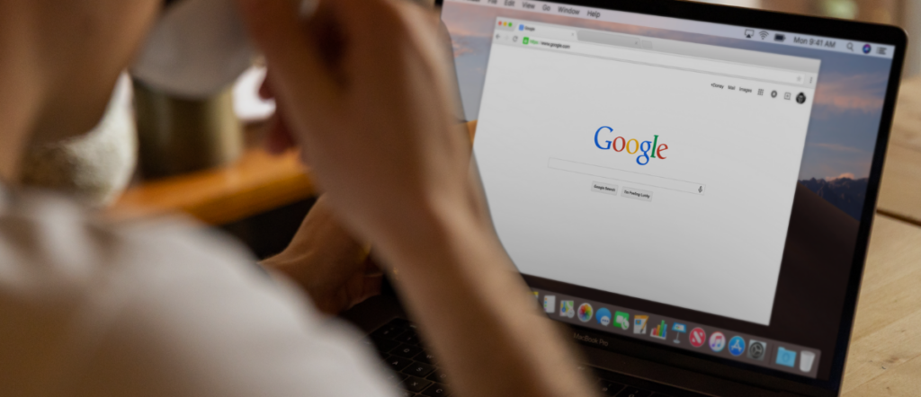 Ein Mensch der gerade dabei ist ein Schluck von einer Tasse zu nehmen und dabei auf dem Laptop die Suchmaschine Google betrachtet.